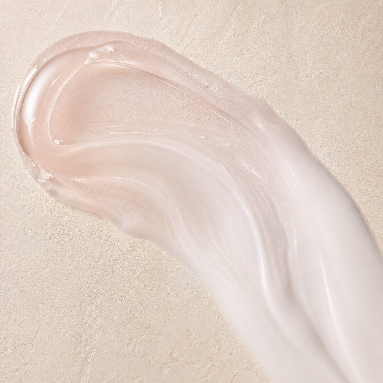 Roséfarbene Textur des Oil-to-Milk Cleansers auf heller Steinfläche.